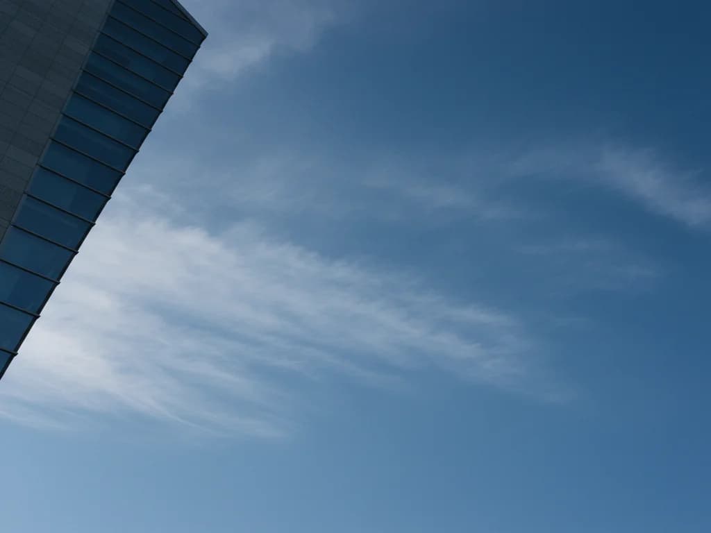 Cielo azul profundo con nubes cirros suaves enmarcado por el borde de una torre modernista